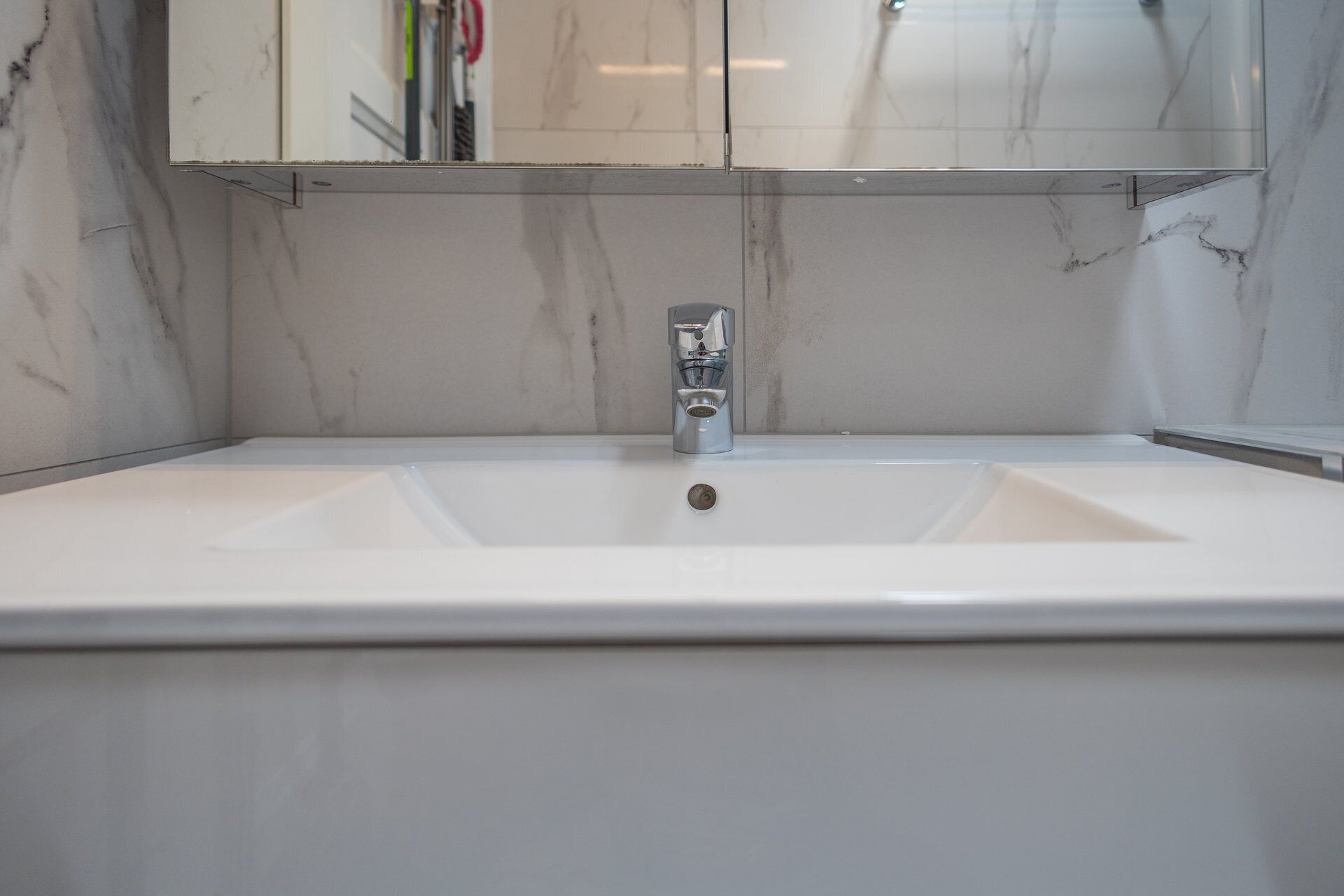 Ein Badezimmer mit einem weißen Waschbecken, einem chromfarbenen Wasserhahn und einem Spiegel darüber.