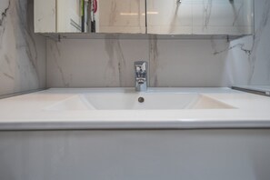 Um banheiro com uma pia branca, uma torneira cromada e um espelho acima.