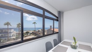 A room with a large window overlooking a beach, a table with a plant, and a chair. - GuestReady - San Agustin Blue Flag Beach (San Agustin)