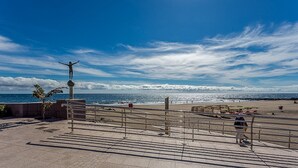 A coastal promenade with a statue, a beach, and a clear sky. - GuestReady - San Agustin Blue Flag Beach (San Agustin)