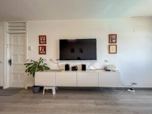 Uma sala de estar moderna com televisão de tela plana na parede, um rack branco, um vaso de planta e obras de arte emolduradas.