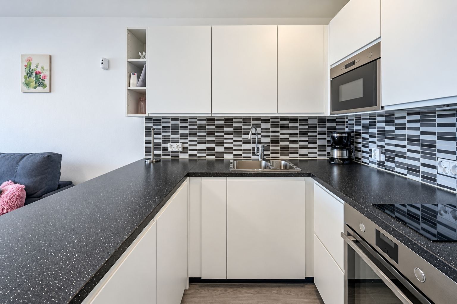 Cozinha moderna com bancada preta, armários brancos, micro-ondas e cafeteira.
