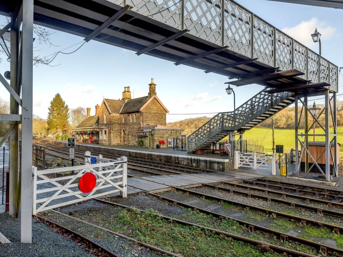 A railway station with a stone building, a pedestrian bridge, and multiple railway tracks.