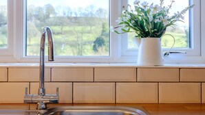 Un lavandino da cucina con un rubinetto moderno, un vaso bianco con fiori sul davanzale e vista sul verde circostante.