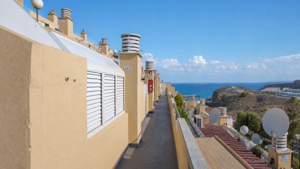 Um caminho estreito entre edifícios, com vista ampla para o mar e terreno rochoso.