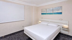 Quarto de hotel com cama, televisão na parede e pintura de uma paisagem praiana.