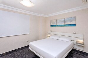 Ein Hotelzimmer mit einem Bett, einem an der Wand befestigten Fernseher und einem Bild einer Strandansicht.