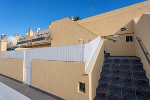 Ein Wohngebäude mit hellbeiger Fassade, einem weißen Zaun und einer Treppe aus Stein, die zu einer Tür führt.