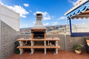 Uma área de churrasco ao ar livre com parede de pedra, um pátio revestido e vista para uma cidade ao fundo.