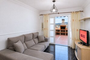 Ein Wohnzimmer mit einem beigefarbenen Sofa, einem Fernseher und Blick auf eine Terrasse mit Grill.