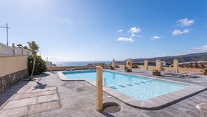Piscina no terraço com água azul cristalina, cercada por espreguiçadeiras e uma vista panorâmica do oceano.