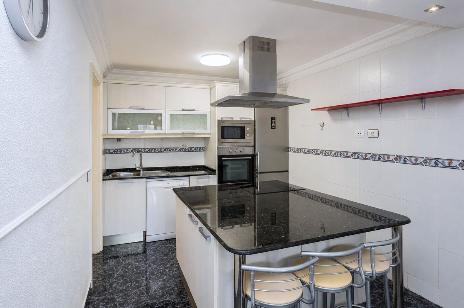 A compact kitchen with a central island, bar stools, a microwave, oven, and a built-in range hood.
