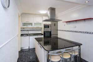 Cozinha compacta com ilha central, banquetas, micro-ondas, forno e coifa embutida.