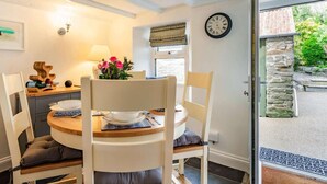 A dining area with a round table, chairs, a clock, and a window with a view of greenery. - 2 Bed in Bodmin (oc-76604) (Saint Mabyn)