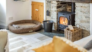 A cozy living room with a stone fireplace, a pet bed, a basket, and a wooden door. - 2 Bed in Bodmin (oc-76604) (Saint Mabyn)
