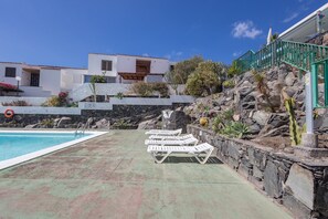 Uma piscina com espreguiçadeiras, um muro de pedra e um edifício com fachada branca.
