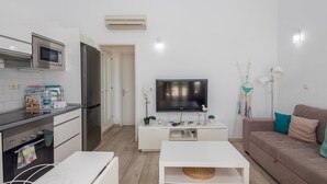 A modern kitchen with a microwave, stove, and refrigerator, a living area with a TV and sofa, and a white console table. - GuestReady - Aguila Beachfront Apartment (San Agustin)