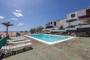 Uma piscina com espreguiçadeiras, um muro de pedra e vista para o mar.