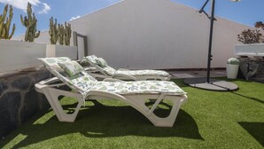 A patio with two white lounge chairs, a white umbrella, and a cactus garden. - GuestReady - Aguila Beachfront Apartment (San Agustin)