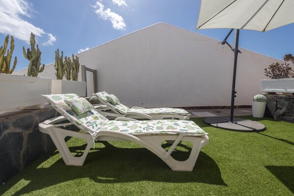 Um pátio com duas cadeiras de descanso brancas, um guarda-sol branco e um jardim de cactos.