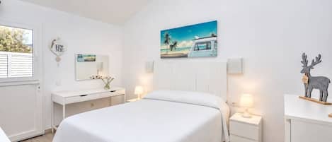 A hotel room with a bed, bedside tables, a dresser, a window with blinds, a painting on the wall, and a decorative reindeer.