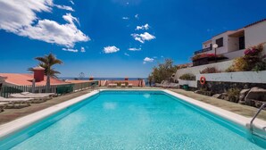 A clear blue pool with lounge chairs, a palm tree, and a view of the sea. - GuestReady - Aguila Beachfront Apartment (San Agustin)