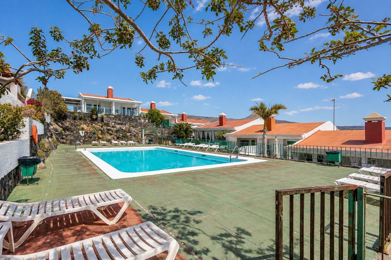 Une piscine avec des chaises longues, un mur en pierre et une vue sur les maisons au loin.