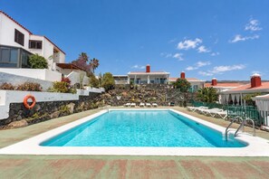 Ein Schwimmbecken mit Liegestühlen und einem Rettungsring, umgeben von einer Steinmauer und Bepflanzung.