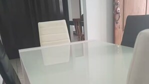 Een kamer met een tafel met glazen blad, een witte stoel en een houten deur.