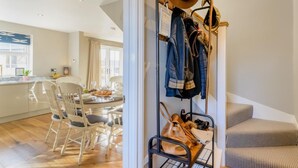 Uma sala de jantar com uma mesa posta para dois, um porta-roupas com chapéus e casacos, e uma escada com um banco acolchoado.