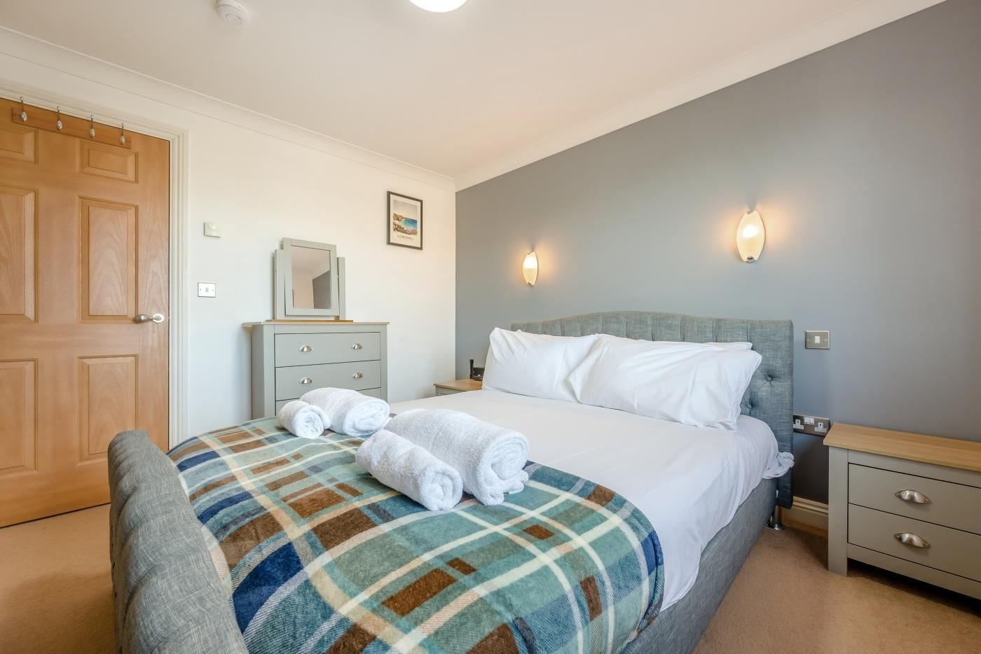 Une chambre d’hôtel avec un lit, une table de chevet, une commode, un miroir et une porte.