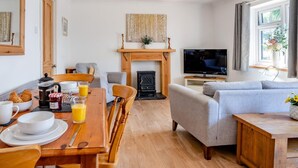 Ein gemütliches Wohnzimmer mit Kamin, einer Essecke mit Frühstücksangeboten, einer Couch und einem Fernseher.