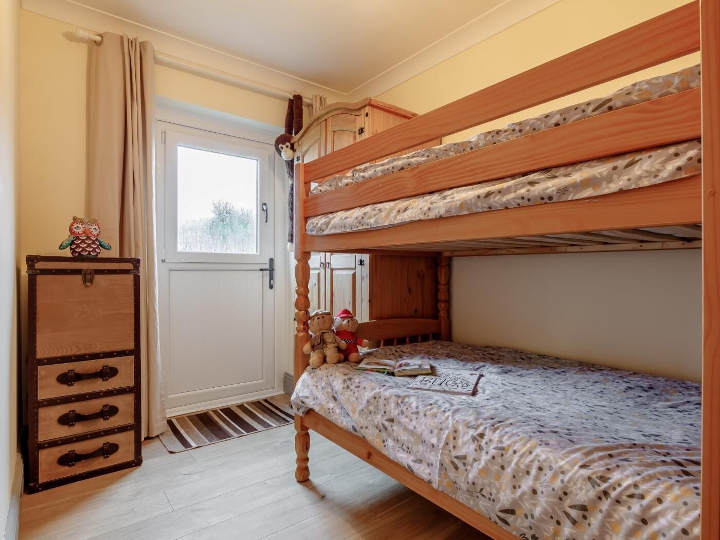 A bunk bed room with a wooden dresser, a small window, and a door.