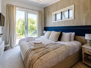 Ein Schlafzimmer mit einem großen Bett, einem Nachttisch, einem Fernseher und einem Fenster mit Vorhängen.