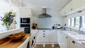 A modern kitchen with white cabinetry, a wooden dining table, and a built-in oven. - 2 Bed in Ludlow (oc-78025) (Richards Castle)