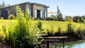 A modern house with a large glass door, a patio with outdoor furniture, and a grassy area. - 2 Bed in Ludlow (oc-78025) (Richards Castle)