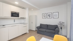 A modern kitchen with white cabinets, a microwave, and a sink. There is a gray sofa and a yellow chair in the living area. - GuestReady - Artiles Near Canteras Beach (Las Palmas de Gran Canaria)