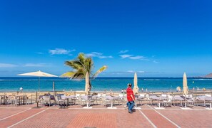 Eine Terrasse direkt am Strand mit Gartenmöbeln und Sonnenschirmen, mit Blick auf den Ozean.