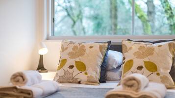 A neatly made bed with rolled towels, two pillows with leaf patterns, and a lamp on a bedside table.