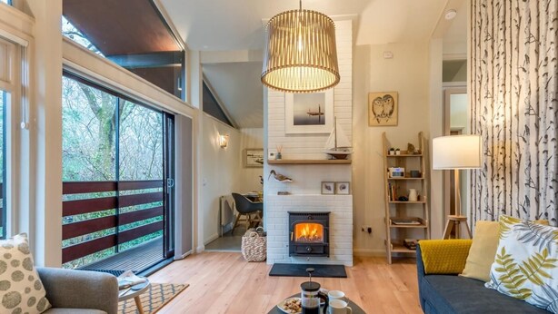Ein modernes Wohnzimmer mit Kamin, Essbereich und großem Fenster mit Blick auf Bäume.