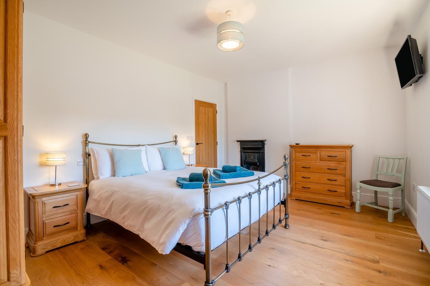 A bedroom with a bed, bedside tables, a dresser, a chair, a fireplace, and a television mounted on the wall.