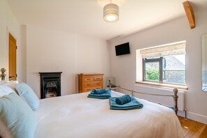 Ein Schlafzimmer mit Bett, einem Holzkapfen, Kamin, Fenster mit Aussicht und einem Wand-Fernseher.
