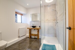 Een moderne badkamer met een douchecabine van glas, een houten wastafelmeubel en een wit toilet.