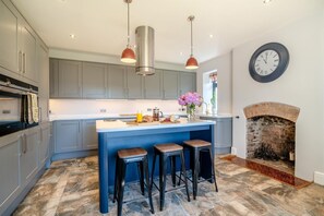 Een moderne keuken met grijze kastjes, een centraal eiland met krukken, hanglampen en een houten haard.