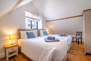 Quarto com duas camas, janela com vista, uma cadeira e mesa de cabeceira com abajur.