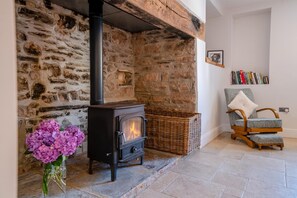 A stone fireplace with a black stove, a wicker basket, a chair with a fluffy pillow, and a vase of flowers. - 5 Bed in Wellington (oc-77900) (Ashbrittle)