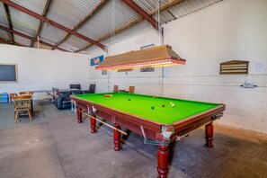 Uma mesa de bilhar numa sala com pé direito alto e um quadro negro na parede.