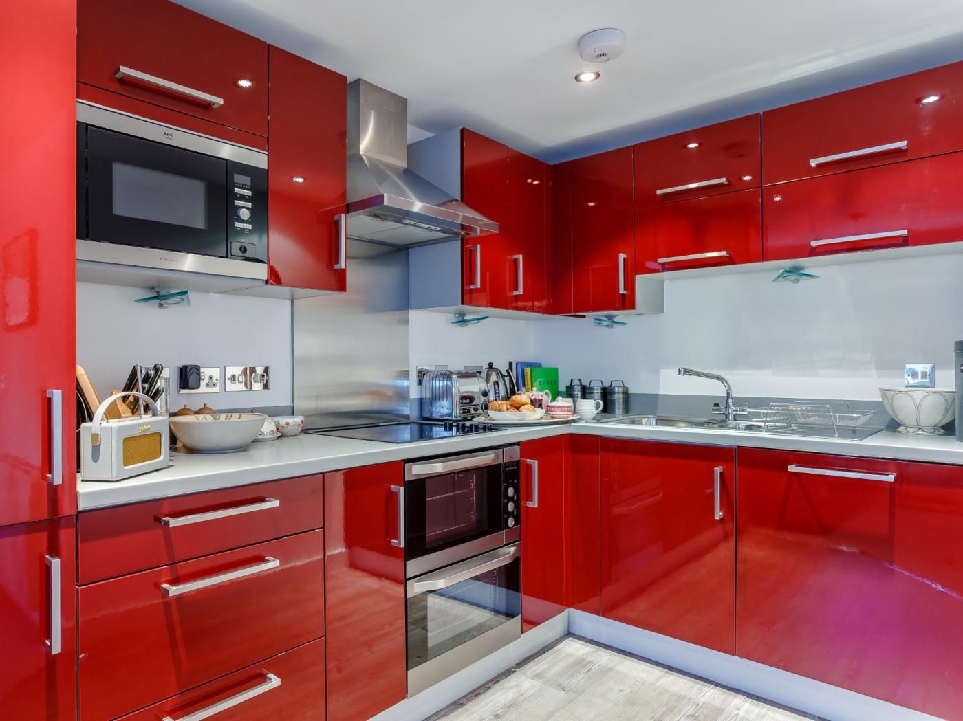 A modern kitchen with red cabinetry, stainless steel appliances, and a glass backsplash.