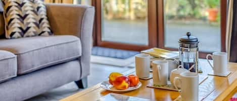 A living room with a sofa, a coffee table with a French press, cups, and a plate of fruit.