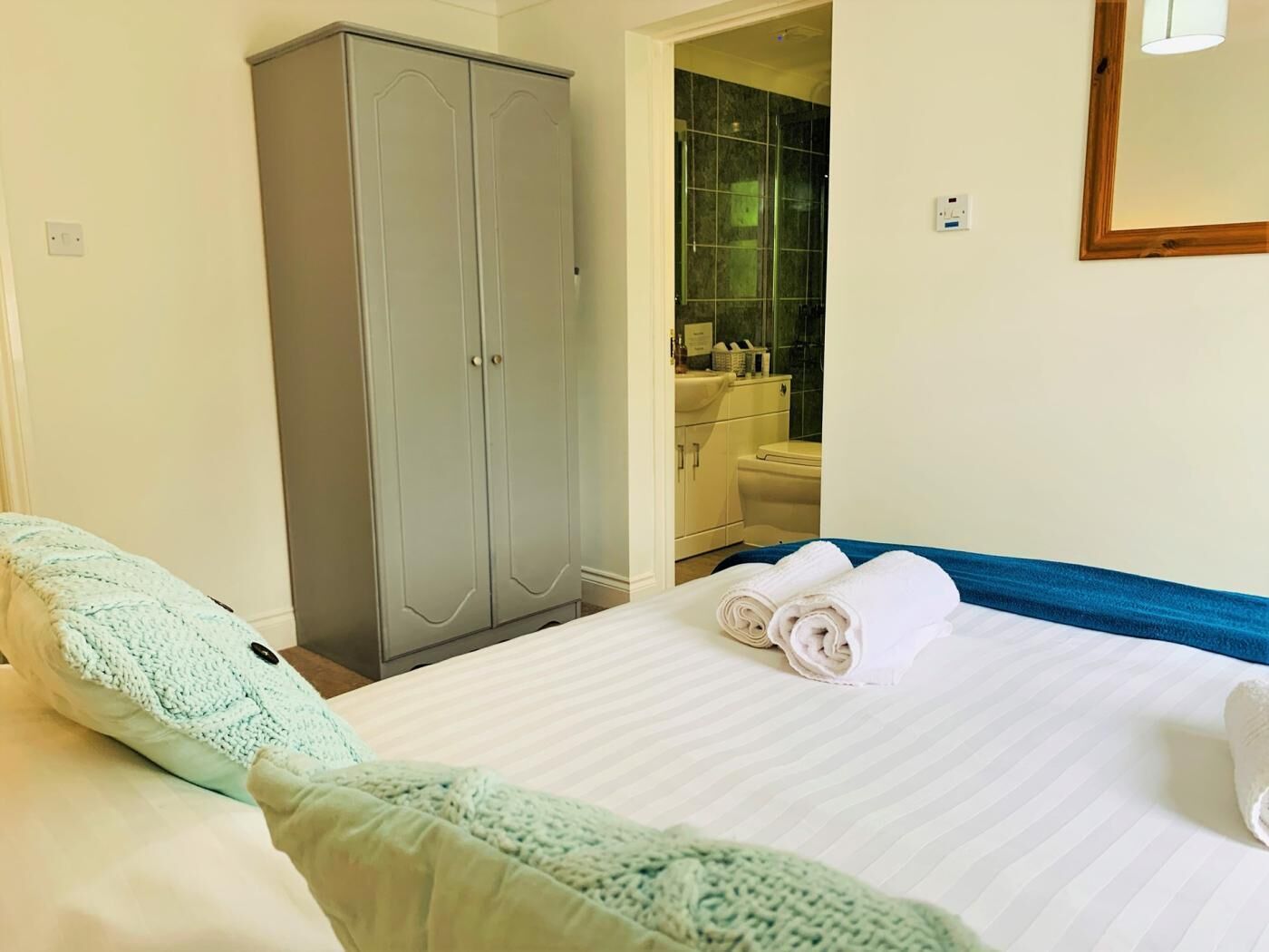 Habitación de hotel con cama, armario, baño con ducha y espejo en la pared.